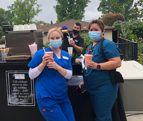 Two nurses are holding cups of drinks outside.